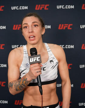 Juliana Miller on a UFC.COM backdrop being interviewed with a microphone featuring UFC branding. 