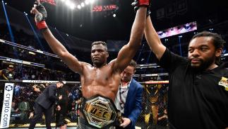 Francis Ngannou comemora com os braços erguidos e vestindo o cinturão após vencer Ciryl Gane no UFC 270