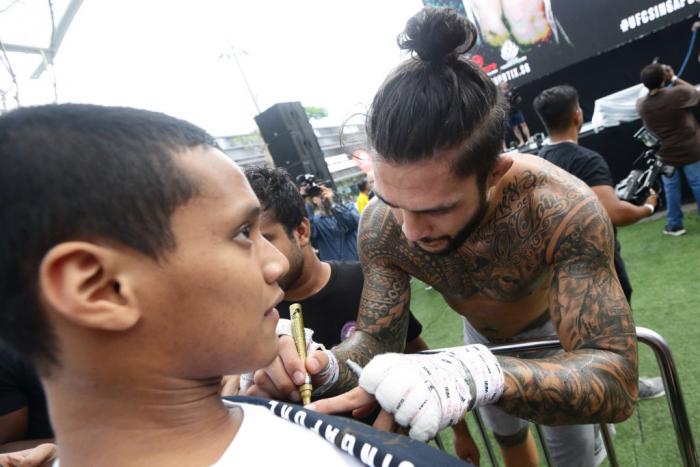 SINGAPORE - JUNE 20:  Tyson Pedro (R) of Australia signs autograph for a fan during the UFC Fight Night Open Workout at OCBC Square on June 20, 2018 in Singapore.  (Photo by Suhaimi Abdullah - Zuffa LLC/Zuffa LLC)