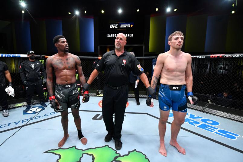 O árbitro Dan Miragliotta segura os braços de Kevin Holland e Kyle Daukaus no centro do Octógono durante o anúncio de luta sem resultado no UFC Vegas 38.